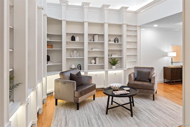 living area featuring ornamental molding, light wood-type flooring, and built in features