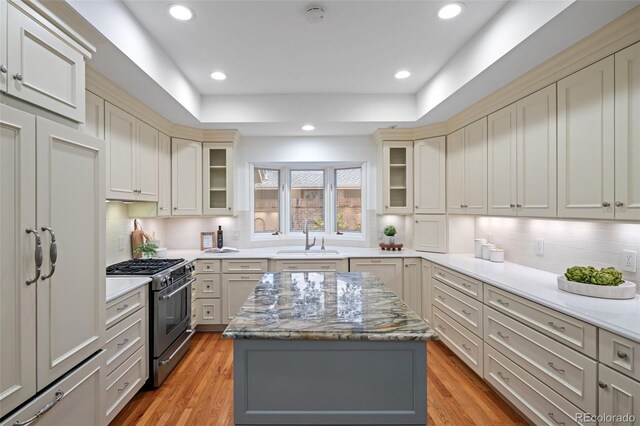 kitchen with stainless steel range with gas cooktop, a sink, backsplash, light wood-type flooring, and recessed lighting