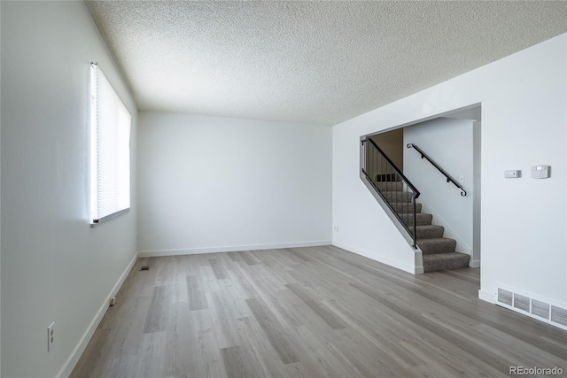 empty room with visible vents, a textured ceiling, wood finished floors, baseboards, and stairs