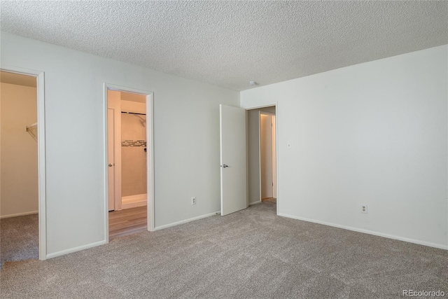 unfurnished bedroom with carpet, a closet, a spacious closet, a textured ceiling, and baseboards