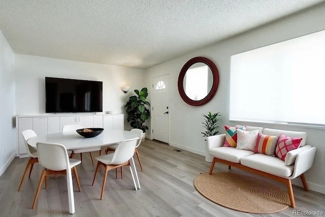dining space featuring baseboards, light wood-type flooring, and a textured ceiling