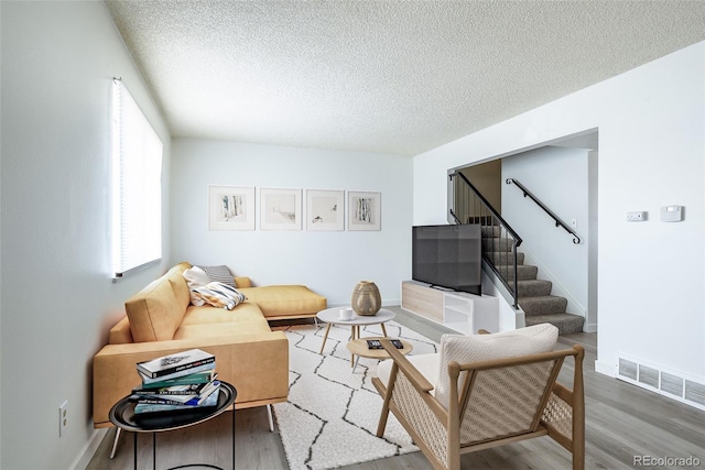 living room featuring a textured ceiling, baseboards, visible vents, wood finished floors, and stairway