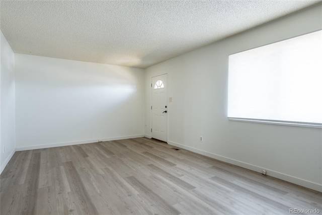 interior space featuring light wood-style flooring, a textured ceiling, and baseboards