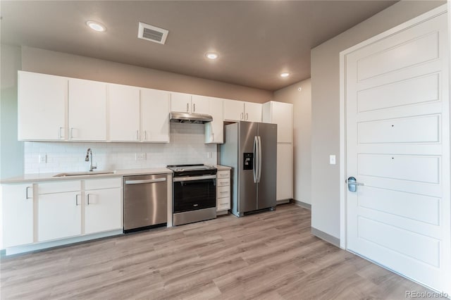 kitchen with appliances with stainless steel finishes, decorative backsplash, sink, white cabinets, and light hardwood / wood-style flooring