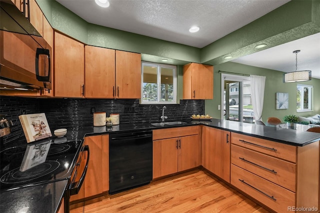 kitchen with black appliances, a sink, a peninsula, tasteful backsplash, and light wood-style floors