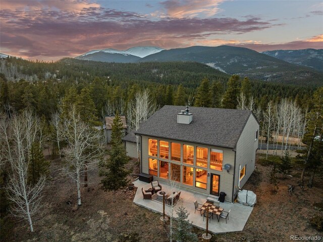 381 Highlands Dr, Bailey, CO 80421 - back of property with a mountain view, a patio, a chimney, a shingled roof, and a forest view