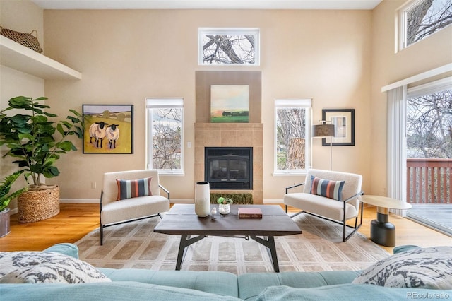 living room featuring baseboards, a tile fireplace, wood finished floors, and a high ceiling