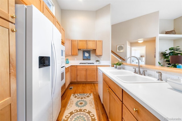 kitchen with light countertops, a sink, white appliances, and light wood-style flooring