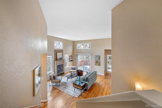 living room featuring light wood finished floors, a textured wall, baseboards, and a fireplace