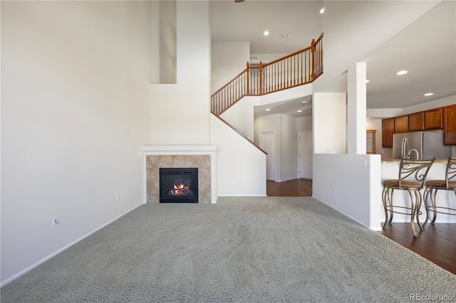 unfurnished living room with a towering ceiling, a tiled fireplace, and dark carpet