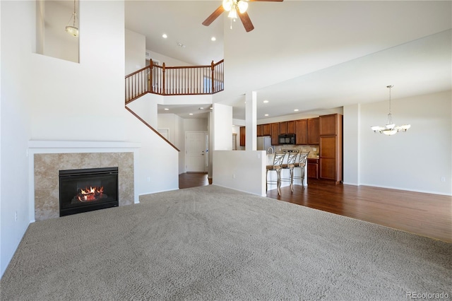 unfurnished living room featuring dark carpet, ceiling fan with notable chandelier, a fireplace, and a towering ceiling