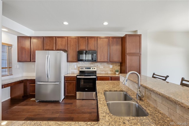 kitchen featuring appliances with stainless steel finishes, sink, dark hardwood / wood-style flooring, a kitchen bar, and light stone countertops