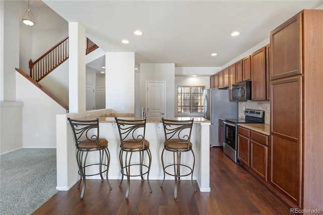 kitchen with light stone counters, stainless steel appliances, a kitchen bar, and decorative light fixtures