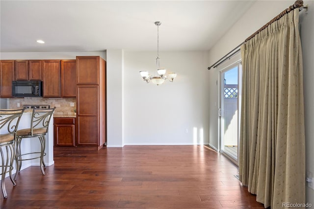 kitchen with a kitchen bar, a chandelier, hanging light fixtures, decorative backsplash, and dark wood-type flooring