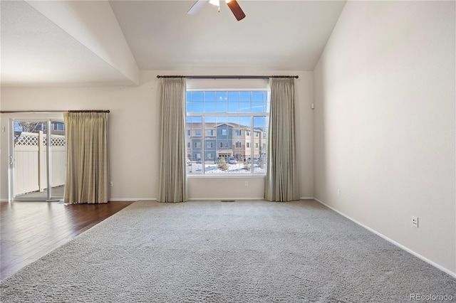 unfurnished room with lofted ceiling, dark carpet, a wealth of natural light, and ceiling fan