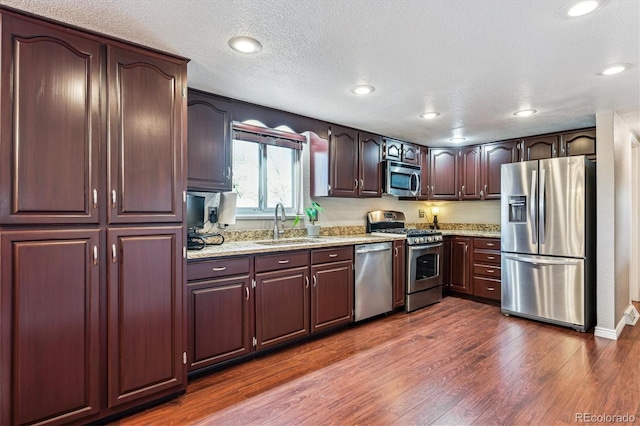kitchen featuring dark wood-type flooring, a sink, light stone counters, a textured ceiling, and stainless steel appliances