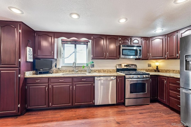 kitchen with dark wood-style floors, appliances with stainless steel finishes, light stone countertops, and a sink