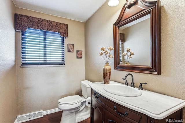 bathroom with vanity, wood finished floors, visible vents, toilet, and a textured wall
