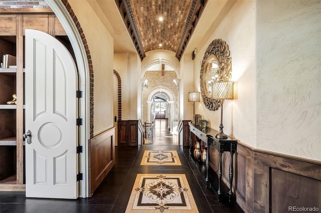 hallway with brick ceiling, dark tile patterned flooring, and lofted ceiling