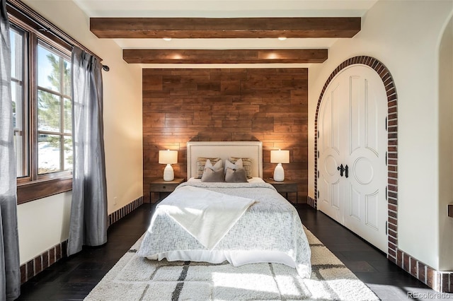 bedroom with beam ceiling, wooden walls, and multiple windows