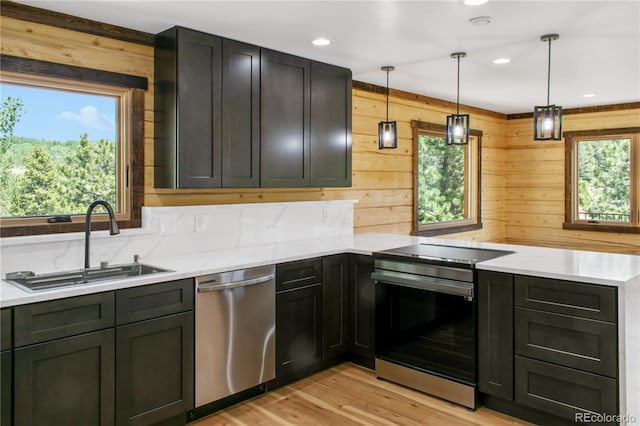 kitchen featuring appliances with stainless steel finishes, pendant lighting, wooden walls, sink, and light wood-type flooring