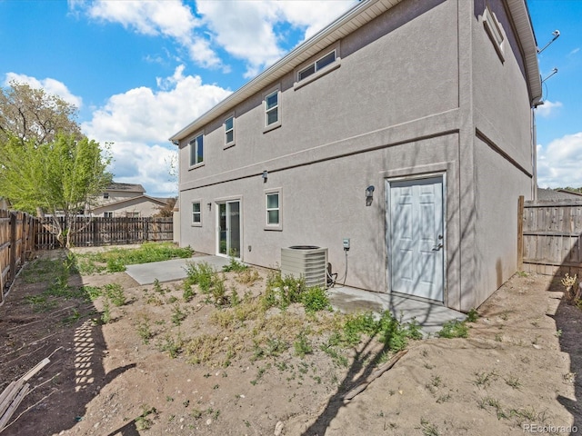 rear view of house featuring stucco siding, a fenced backyard, central AC unit, and a patio
