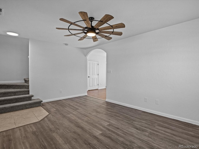 unfurnished living room with a ceiling fan, arched walkways, baseboards, stairs, and dark wood-style flooring