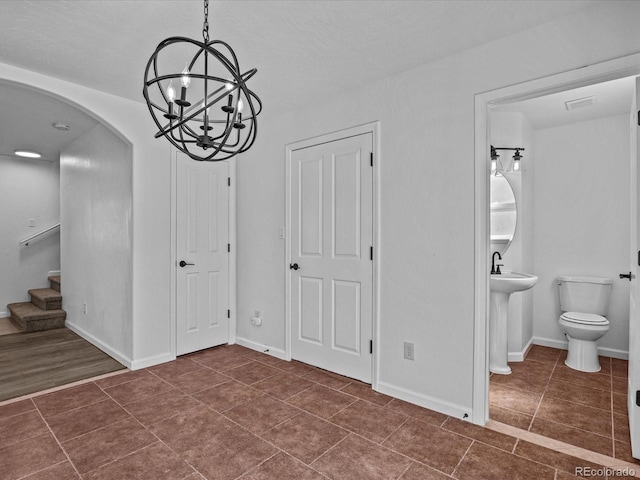 unfurnished dining area with arched walkways, an inviting chandelier, dark tile patterned floors, and stairs
