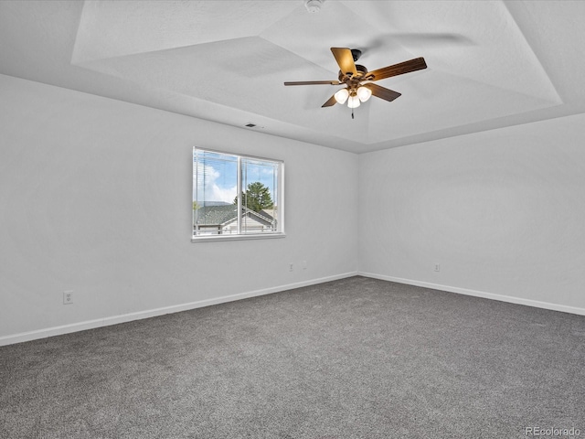 carpeted empty room featuring visible vents, a ceiling fan, baseboards, and a raised ceiling