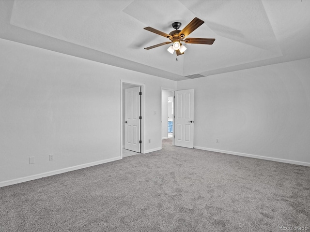 spare room featuring a raised ceiling, carpet flooring, a ceiling fan, and baseboards