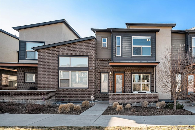 view of front of home with covered porch, brick siding, and stucco siding