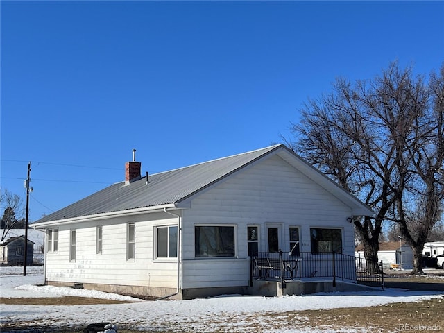 exterior space featuring metal roof, a porch, and a chimney