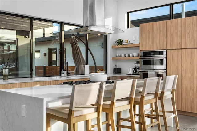 kitchen featuring double oven, a breakfast bar area, island range hood, modern cabinets, and open shelves