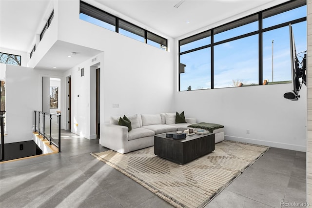 living area featuring plenty of natural light, visible vents, baseboards, and a towering ceiling