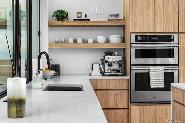 kitchen featuring open shelves, double oven, light stone counters, modern cabinets, and a sink