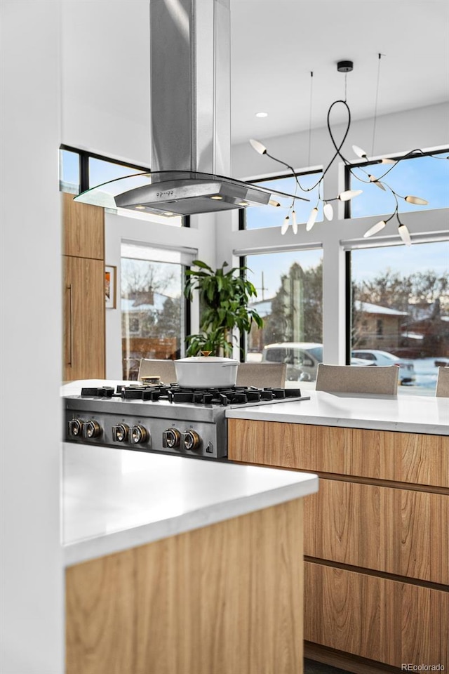 kitchen with island range hood, light countertops, brown cabinets, stainless steel gas stovetop, and modern cabinets