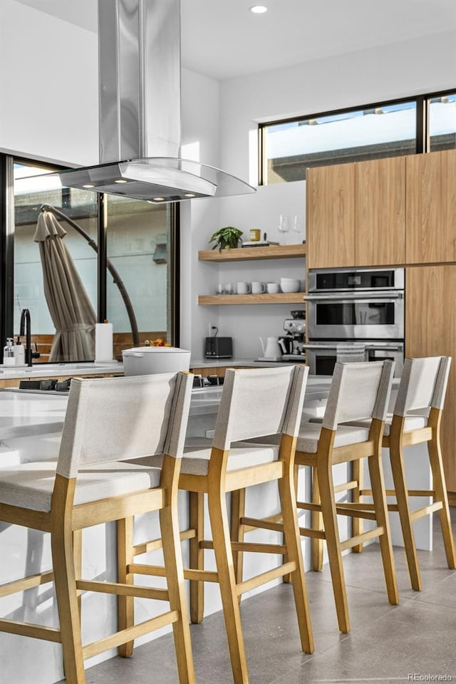 kitchen with modern cabinets, light brown cabinets, open shelves, stainless steel double oven, and island range hood