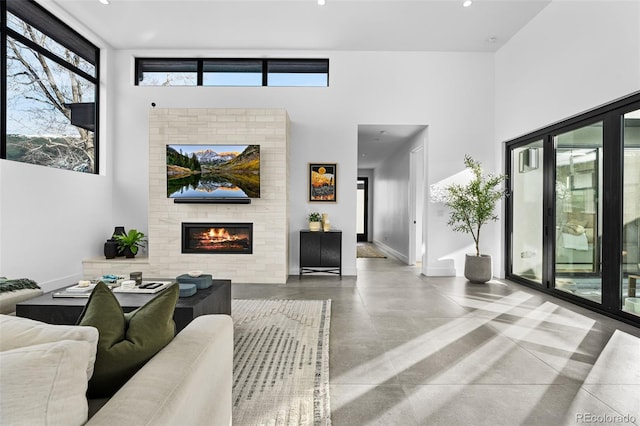 living room featuring finished concrete floors, a brick fireplace, baseboards, and a towering ceiling