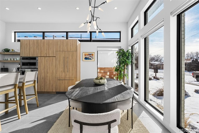 dining space featuring recessed lighting, a notable chandelier, finished concrete floors, and a towering ceiling