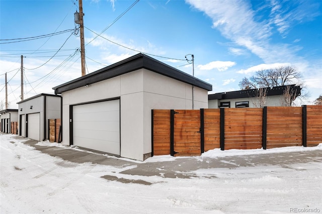 snow covered garage with a detached garage and fence