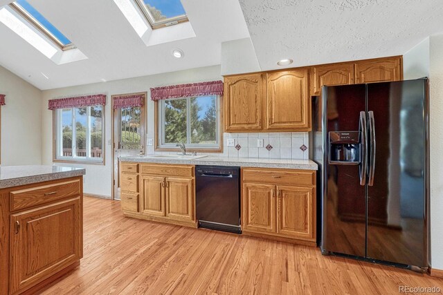 kitchen featuring light wood-type flooring, sink, black appliances, backsplash, and lofted ceiling with skylight