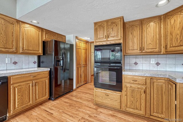 kitchen featuring decorative backsplash, black appliances, light hardwood / wood-style floors, and a textured ceiling