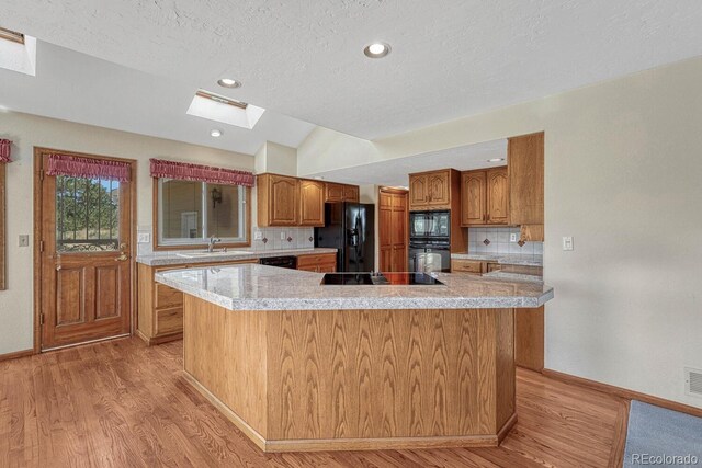 kitchen with black appliances, a center island, lofted ceiling with skylight, and backsplash