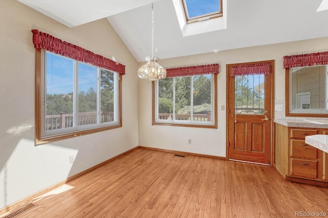 unfurnished dining area featuring vaulted ceiling with skylight, light wood-type flooring, and a chandelier