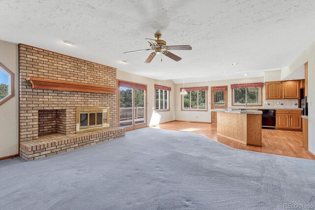 kitchen featuring a brick fireplace, dishwasher, light wood-type flooring, a textured ceiling, and ceiling fan