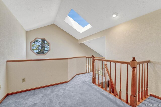 interior space featuring vaulted ceiling with skylight, carpet, and a textured ceiling