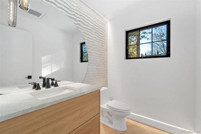 bathroom with vanity, toilet, baseboards, and visible vents