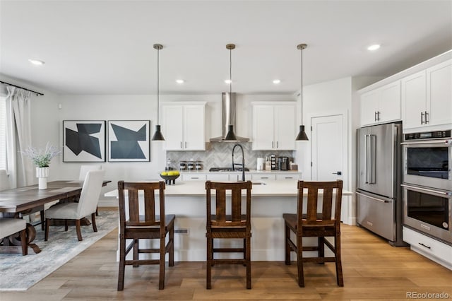 kitchen with decorative backsplash, light countertops, white cabinets, appliances with stainless steel finishes, and wall chimney range hood