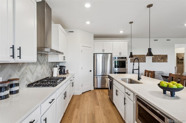 kitchen with appliances with stainless steel finishes, light countertops, wall chimney exhaust hood, and a sink