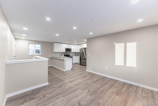 kitchen featuring white cabinets, open floor plan, a peninsula, stainless steel appliances, and light countertops